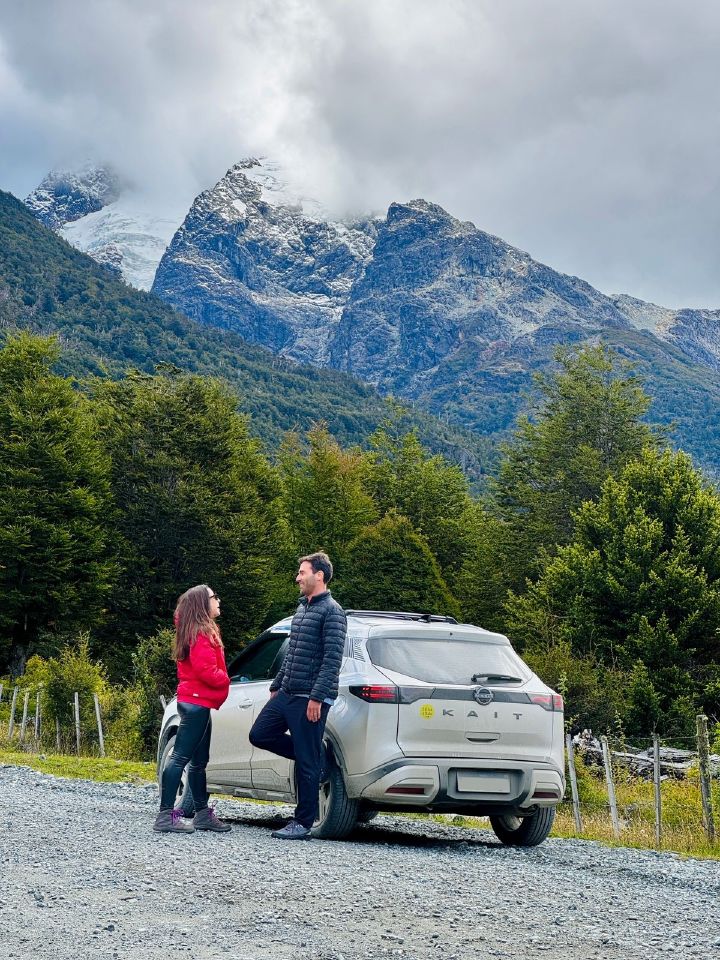 O casal Camila e Guilherme junto ao Nissan Kait parado na estrada Carretera Austral com a Patagônia Chilena ao fundo
