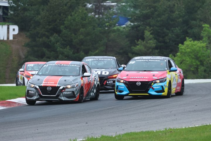 Four Nissan Sentra race cars on the CTPM racetrack driving closely together around a bend with trees in the background