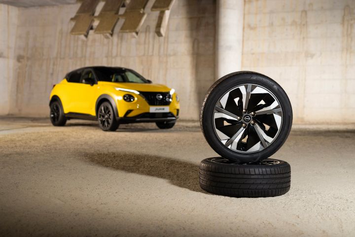 Gelber Nissan Juke 3/4 Front auf hellem Untergrund im Hintergrund und davor zwei Reifen mit silbernen Leichtmetallfelgen