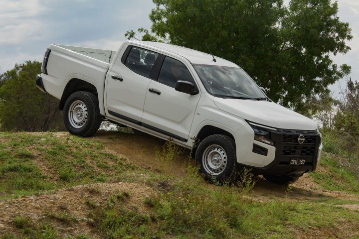 An Alpine White 2026 Nissan Navara parked on an dirt and grass incline front facing downhill.