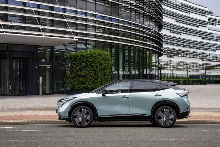 Seitenansicht eines hellblauen Nissan Ariya am Straßenrand vor verschiedenen Bürogebäuden