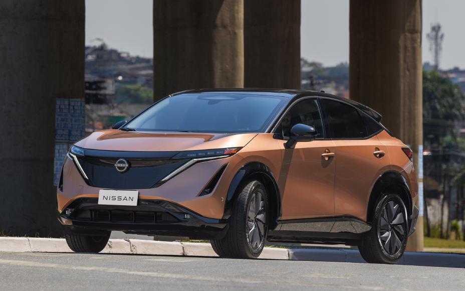 Nissan Aryia na cor cobre estacionado de frente, de três quartos, à frente de colunas de suporte de uma ponte