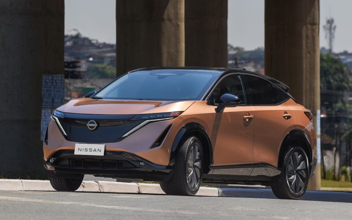 Nissan Aryia na cor cobre estacionado de frente, de três quartos, à frente de colunas de suporte de uma ponte