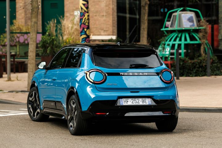 3/4 Heckansicht eines blauen Nissan Micra vor einem städtischen Hintergrund im Zentrum von Rotterdam