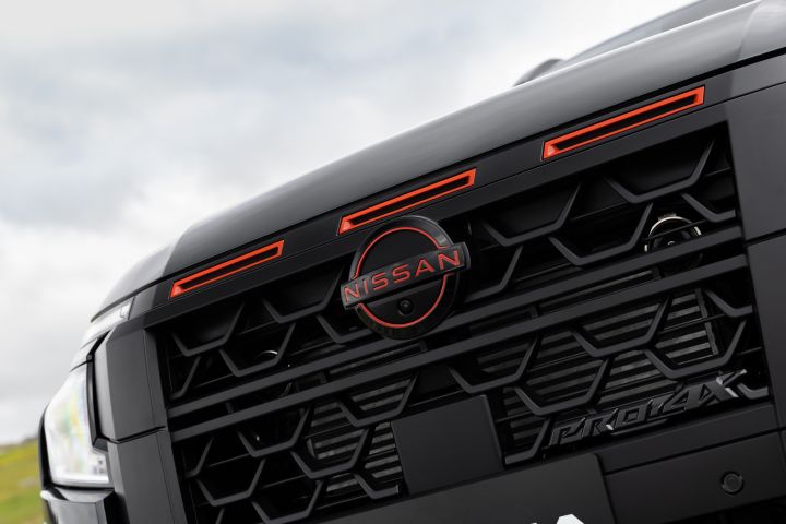2026 Nissan Navara PRO-4X finished in Boulder Grey showing an angled front grille close-up with Nissan badge, red accents and PRO-4X branding.