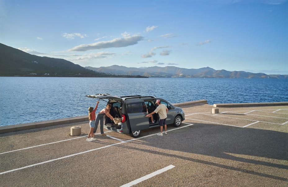 Nissan Townstar Evalia vista desde arriba y con plano lateral trasero en una carretera con mar de fondo, pero con familia abriendo puerta y maletero