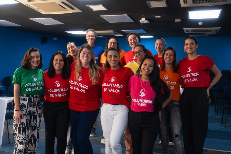 Voluntários em grupo ao lado um do outro posando para foto usando a camiseta do programa ‘’Voluntários de Valor’’