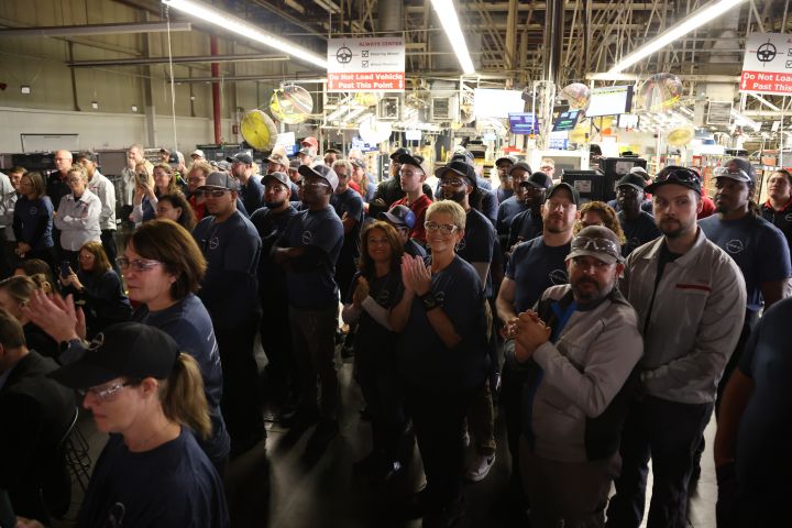 A crowd of Nissan workers standing in a warehouse clapping.