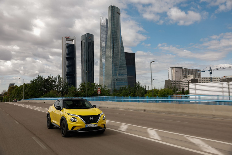 Image dynamique d’un Juke Hybrid jaune en ligne droite avec des tours en arrière plan