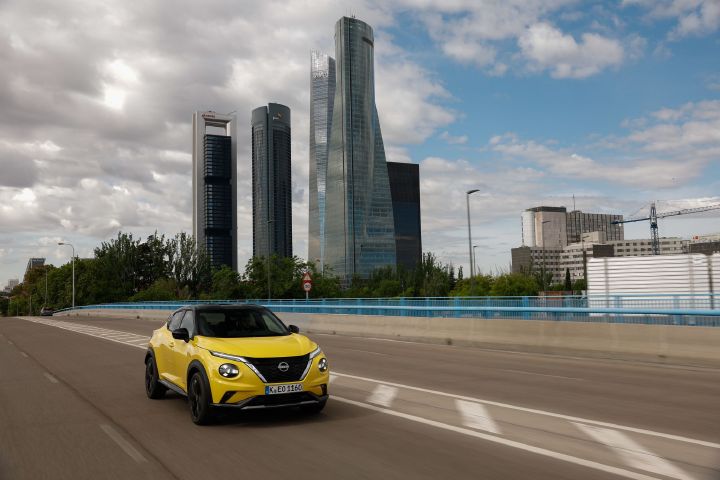 Image dynamique d’un Juke Hybrid jaune en ligne droite avec des tours en arrière plan