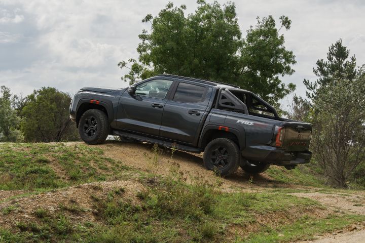 2026 Nissan Navara PRO-4X finished in Boulder Grey side‑hill traversing a grassy mound with sports bar, black alloys and slight wheel lift.