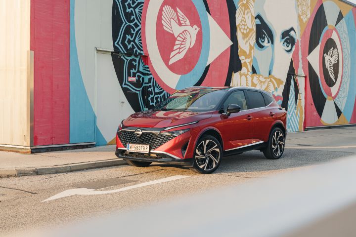 Vor einer Wand mit einem mehrfarbigen Grafitti-Kunstwerk steht ein Nissan Qashqai in Fuji Sunset Red