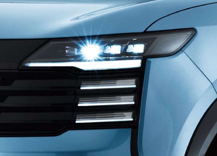 Close-up of the Nissan Kicks headlights illuminated on a bluish model. The horizontal lighting and front grille are emphasized.