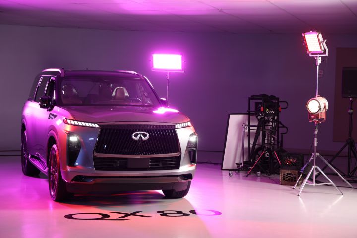 A 2025 INFINITI QX80 parked in a room with pink photo lights shining on it.