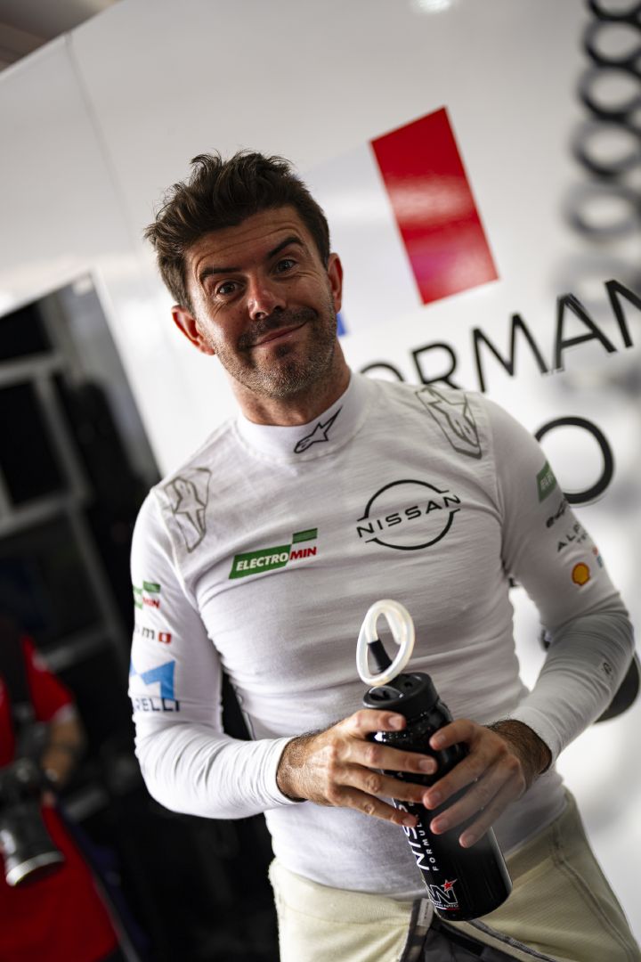 Porträtfoto eines lächelnden Norman Nato in der Teamgarage, in den Händen hält er eine große Trinkflasche
