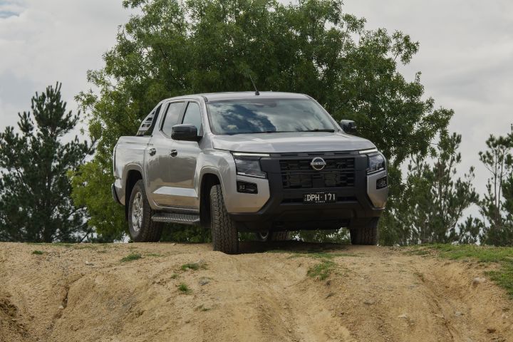 2026 Nissan Navara ST dual cab ute finished in Summit Silver photographed from the rear three-quarter angle descending a dirt embankment.