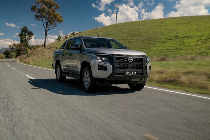 2026 Nissan Navara ST dual cab ute finished in Summit Silver shown driving from a front three-quarter angle on a winding country road.