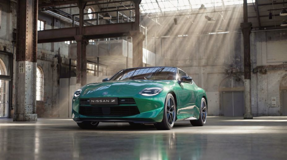 Front three-quarter view of a 2026 Nissan MY26 Z Coupe finished in Unryu Green, parked inside a heritage industrial building with sunlight streaming through overhead windows and reflecting across the polished floor.