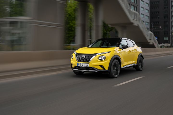 Jadący żółty Nissan Juke (widok z półprofilu) z budynkami w tle