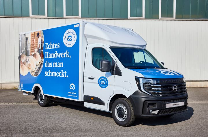 Blick von schräg vorne auf den parkenden Nissan Interstar-e mit blau-weißer Beklebung auf dem Bäckereikoffer und dem Schriftzug "Echtes Handwerk, das man schmeckt".