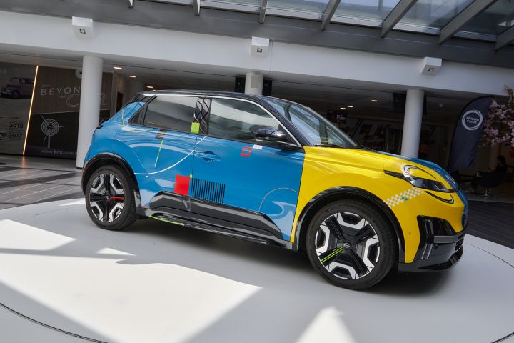 3/4 Frontansicht des blauen Nissan Micra Signature Edition Gewinnerfahrzeugs mit elektrischem Antrieb, schwarzem Dach, auffälligen roten, gelben und schwarzen grafischen Akzenten sowie sportlichen Felgen, ausgestellt in einem weißen Kreis.