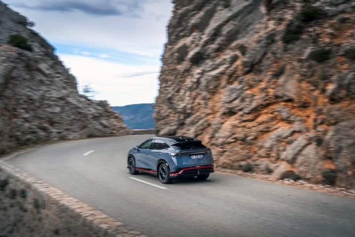 Vue dynamique du ¾ arrière de l'Ariya NISMO à l'approche d'un virage sur une route de montagne.