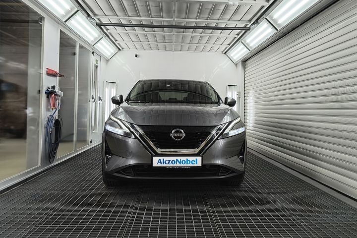 Nissan Qashqai przodem w komorze lakierniczej, z logo Akzo Nobel na tablicy rejestracyjnej