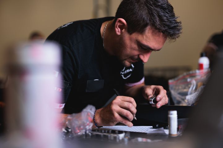 Ein Nissan Formel E Mechaniker hält in der linken Hand ein Bauteil und notiert mit der rechten Hand etwas auf Papier