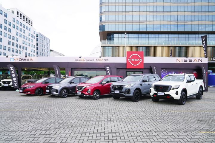 A lineup of Nissan vehicles, including the Leaf, Kicks e‑POWER, Livina, Terra, and Navara, parked in front of a Nissan brand pavilion at an outdoor event.
