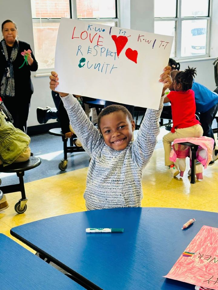 A young boy holding up a hand drawn sign that reads “Love, respect, unity.”