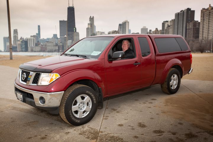 A smiling man in a red Nissan Frontier parked with the Chicago skyline in the background.
