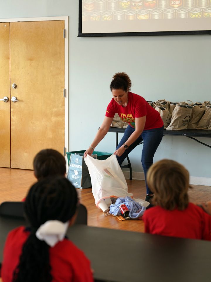 A Nissan employee dumps a bag of items onto the floor in front of seated children.