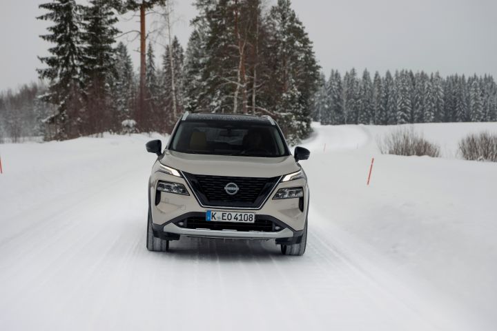 Silberner Nissan X‑Trail e‑Power e‑4ORcE fährt auf schneebedeckter Straße mit verschneiten Bäumen und Schneehaufen auf beiden Seiten, Front