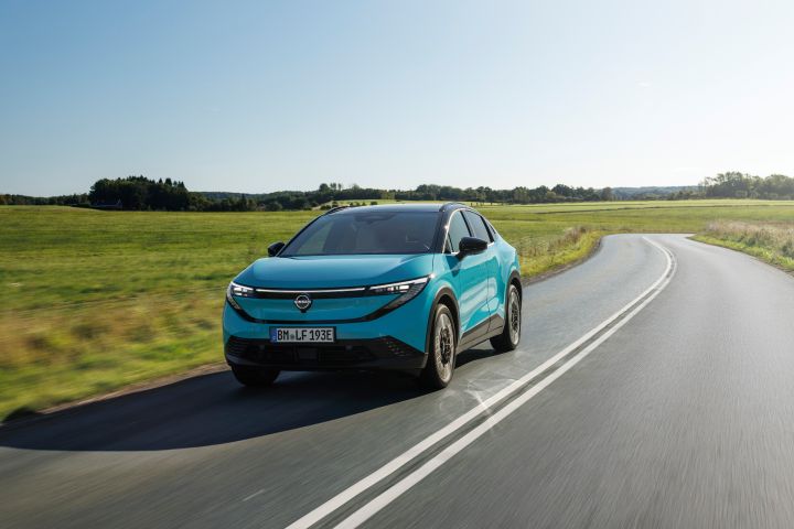 Blick von schräg vorne auf einen türkisen Nissan LEAF, der über eine Landstraße fährt