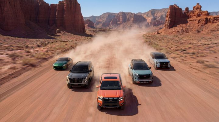 Five Nissan vehicles driving on a desert road in an arrow formation, a dust cloud follows behind each vehicle.