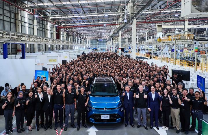 A large group of Nissan employees and executives stand together inside a vehicle manufacturing plant, posing behind the all-new Nissan Kicks e POWER displayed at the front of the production line during the start-of-production ceremony