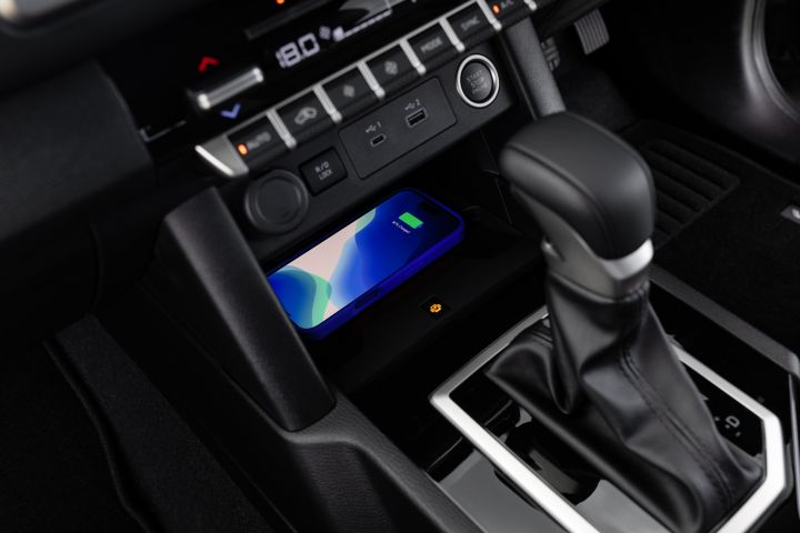 Lower centre console of a 2026 Nissan Navara ST-X showing a smartphone resting on the wireless charging pad, the automatic gear selector, and the climate-control panel above.