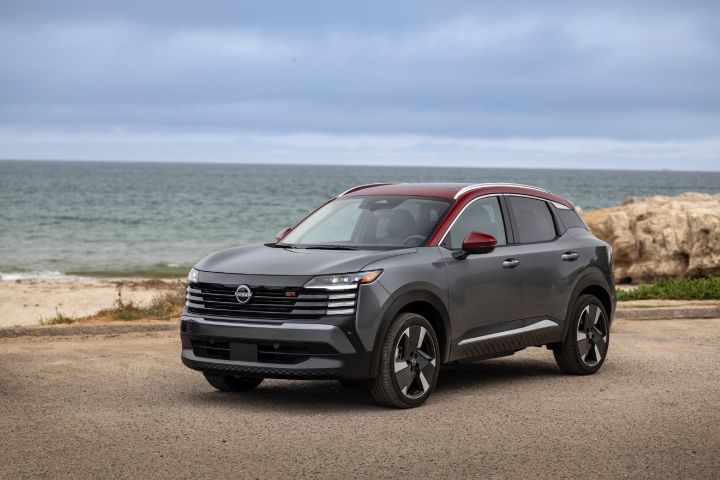 Front right 3/4 angle of a silver 2026 Nissan Kicks parked on a gravel lot overlooking the ocean on a cloudy day.