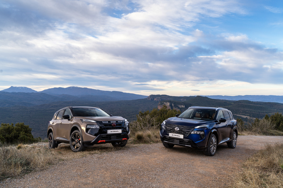 Deux nouveaux 2026 Nissan X‑Trail sont garés sur une route non goudronnée, avec en toile de fond des montagnes et un ciel nuageux. Les véhicules se distinguent par leur design moderne et sont peints dans les couleurs extérieures « Baja Storm » et « Universal Blue », qui soulignent leur robustesse tout-terrain et leur style.