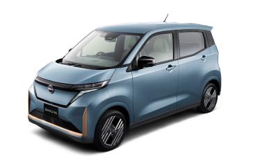 淡いブルーの「日産サクラ」を、無地の白背景の前で車両の左前方から斜めに撮影した画像。コンパクトなボディとフロント周りの造形が際立っている。