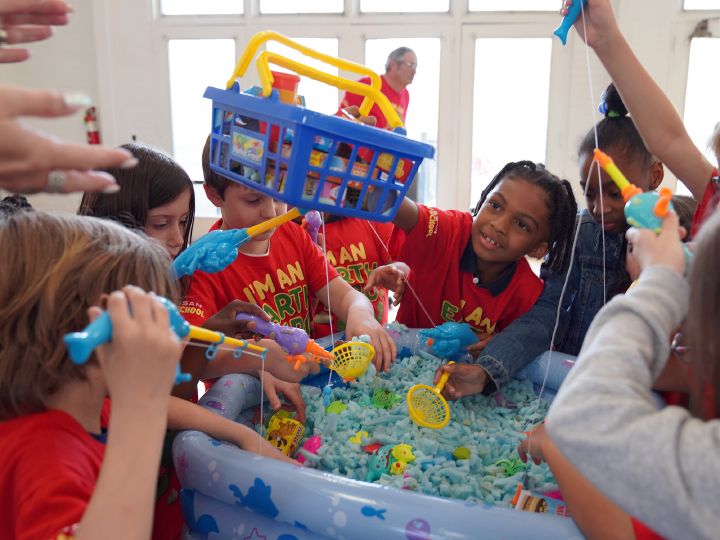 A group of children stand over a play fishing pool, one child holds a basket over top.