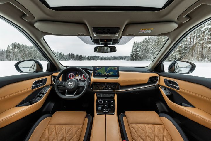 Innenraum des Nissan X‑Trail e‑Power e‑4ORCE mit hellbrauner Lederausstattung, Blick auf Cockpit und Vordersitze, durch die Fenster sieht man eine verschneite Landschaft
