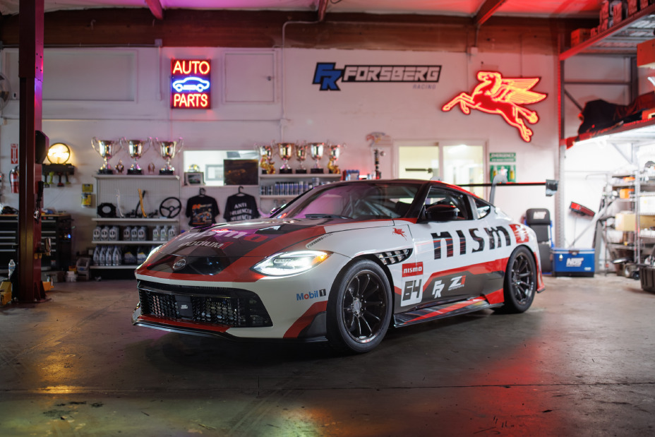 Front left 3/4 view of the Forsberg Racing NISMO GT-Z SEMA build parked in a garage with neon signs hung on the walls.