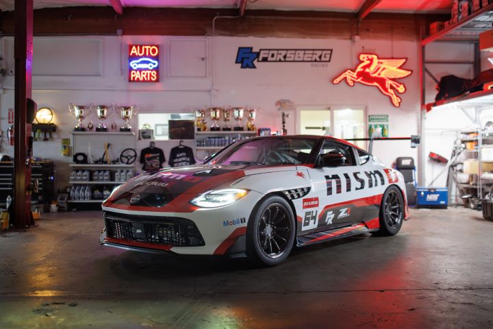 Front left 3/4 view of the Forsberg Racing NISMO GT-Z SEMA build parked in a garage with neon signs hung on the walls.