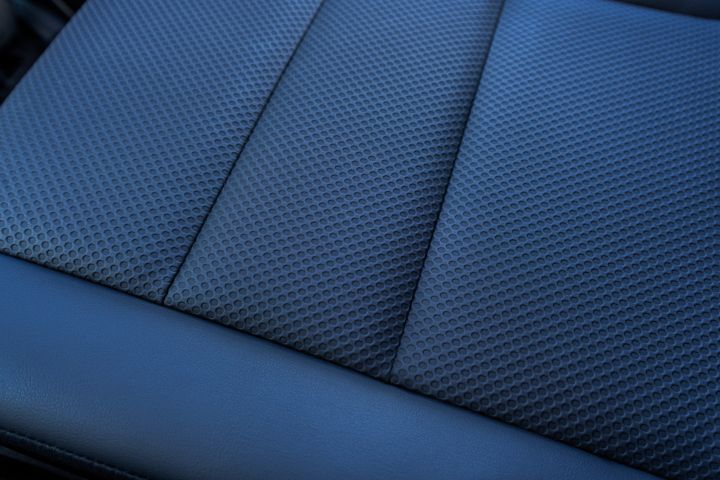 Nahaufnahme des dunklen blauen Autositzes des neuen 2026 Nissan X‑Trail N-Trek mit strukturiertem Wabenmuster auf den Stoffteilen und glatter Lederverkleidung entlang der Kanten. Das Bild hebt den Kontrast zwischen den Materialien und die detaillierten Nähte hervor, die die gepolsterten Segmente voneinander trennen.