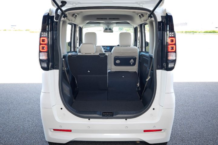 The new Nissan Roox kei car with its rear door open. Inside the white vehicle, the back seats are partially folded down, revealing a layout that allows for expanded cargo space.