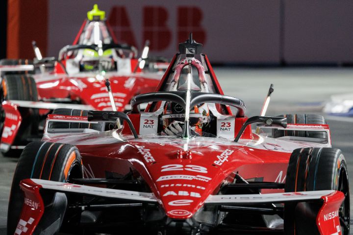 Ein rot-weißer Nissan Formel-E-Rennwagen fährt auf die Kamera zu. Im Cockpit ist Norman Nato zu sehen, hinter ihm folgt ein weiterer Nissan Formel-E-Rennwagen. Die Szene spielt auf einer Rennstrecke, im Hintergrund ist das ABB-Logo zu erkennen.
