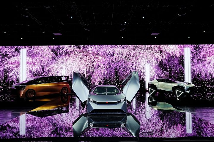 Drei Nissan-Konzeptfahrzeuge auf der Bühne des Nissan-Standes auf der Tokyo Mobility Show 2023. Große Bilder von rosa Kirschblüten werden auf den Boden und die Wände projiziert.