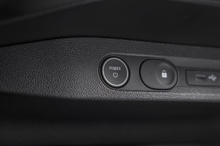 Photograph of vehicle interior door-panel controls, showing a round POWER button, adjacent lock button with white padlock icon, and USB port. Black textured trim and illuminated control symbols indicate power and locking functions.