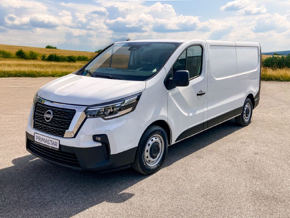 Dreiviertelansicht auf einen weißen Nissan Primastar mit Kühlfahrzeugausbau. Im Hintergrund sind grüne Wiesen zu sehen